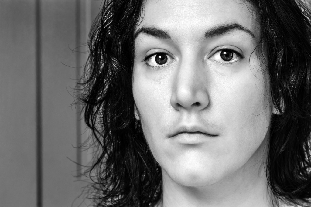 Greyscale self portrait of fair skinned woman with chin length curly dark hair and dark eyes