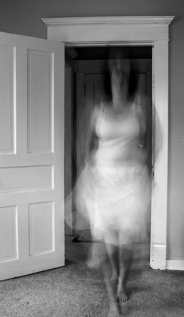 A greyscale image of a curvy brunette in a white dress in motion, blurring her face and features