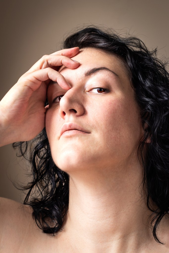 Color self portrait of fair skinned woman with chin length curly dark hair and dark eyes with a hand cupping the right side of her face