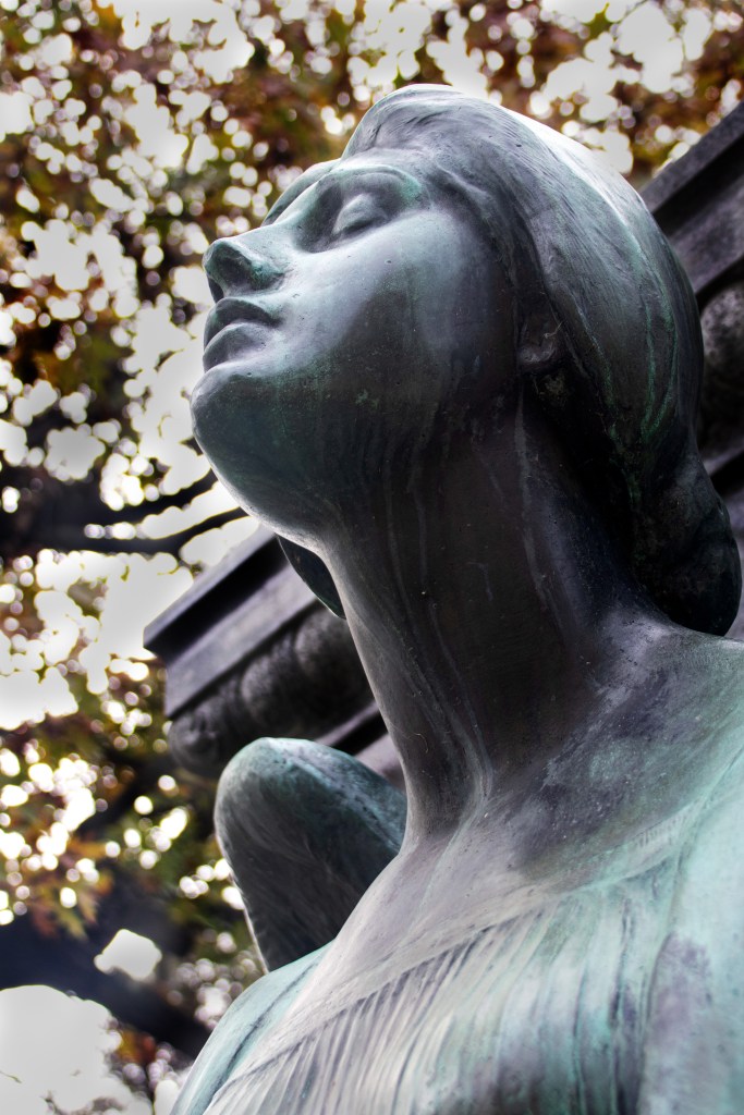 The closeup of the face of a dark green aged bronze angel statue