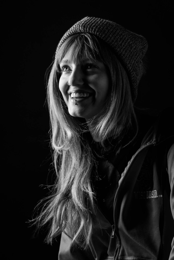 Fair skinned woman with long slightly wavy hair smiles off camera, wearing a hat