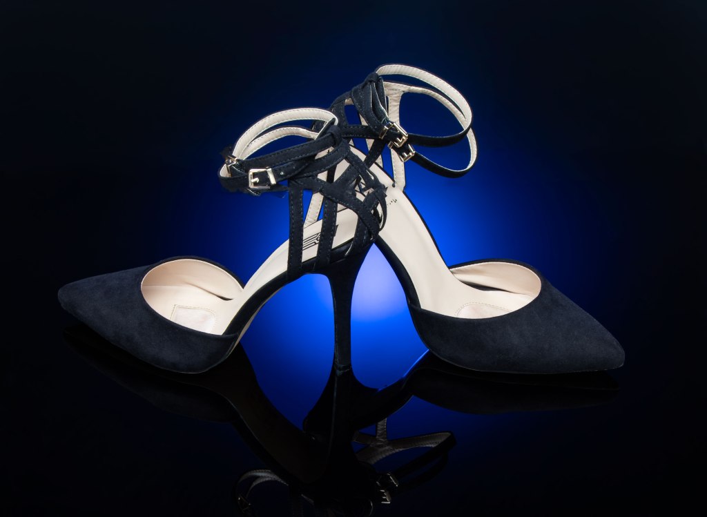 Black velvety strappy stilettos lit with blue light on a black background