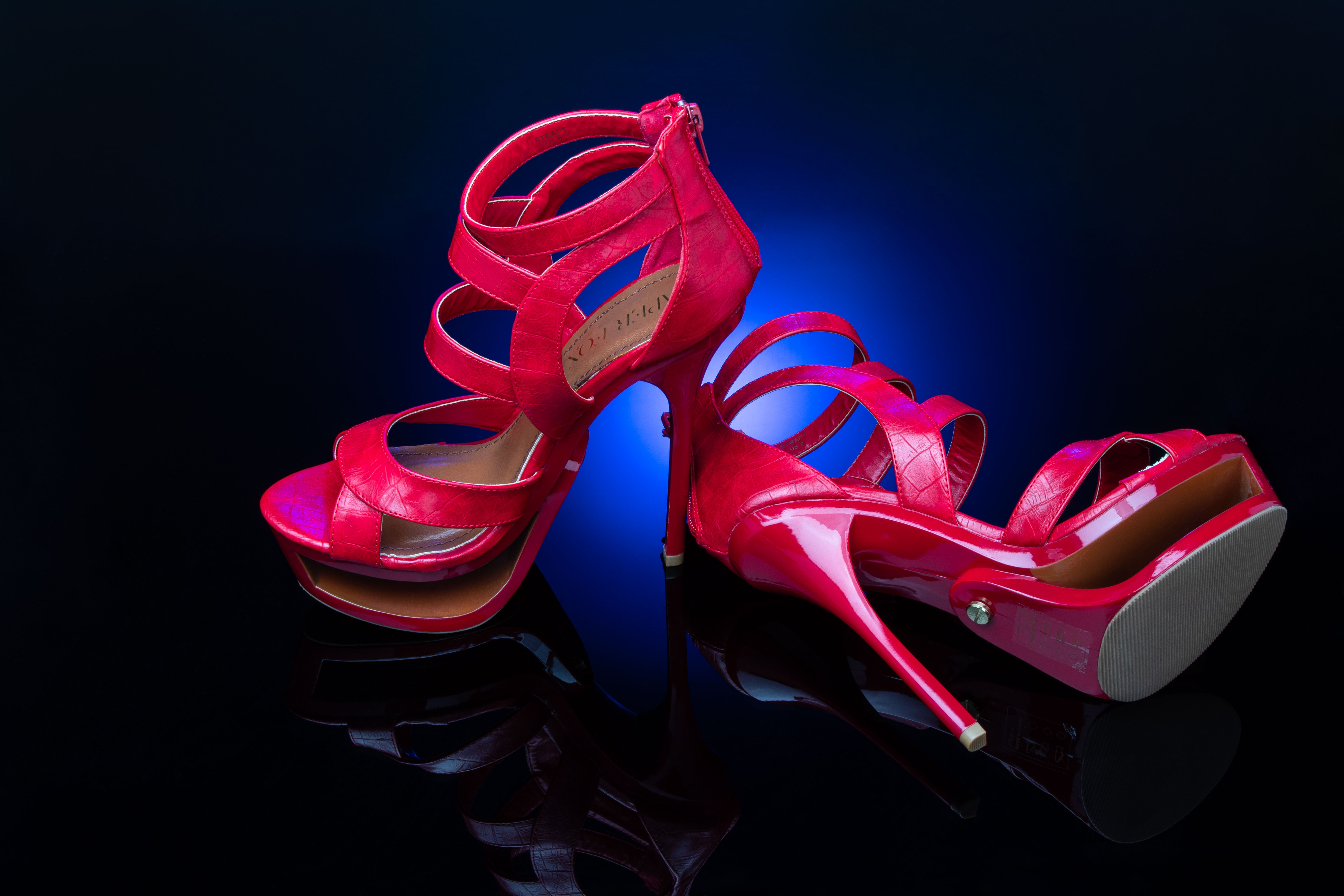 Red strappy stilettos light with blue light on a black background